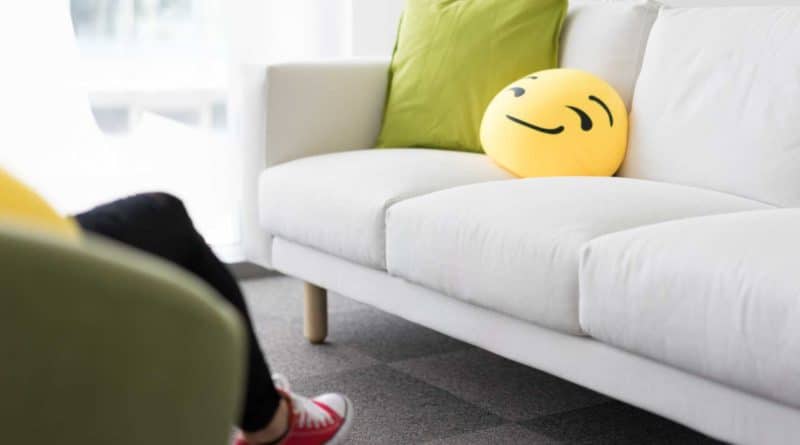 White sofa with a green pillow and a smiling emoji cushion in a bright room.