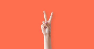 Hand showing a peace sign against a bright orange background.