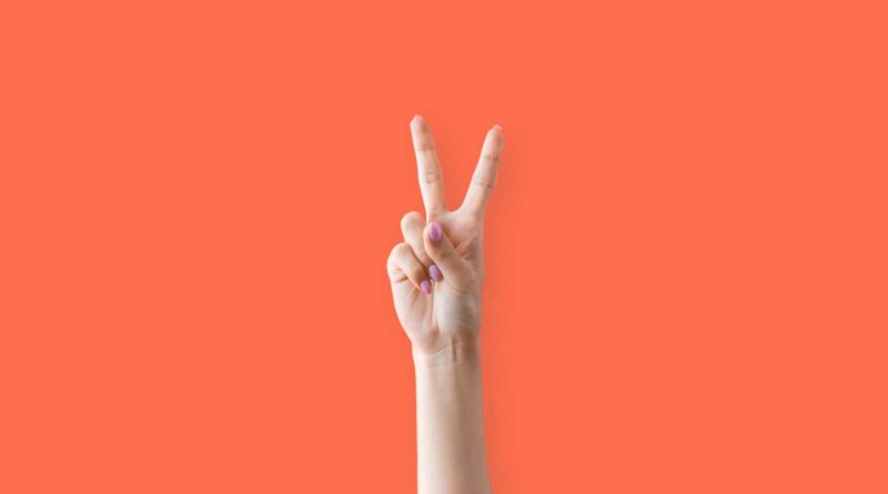 Hand showing a peace sign against a bright orange background.