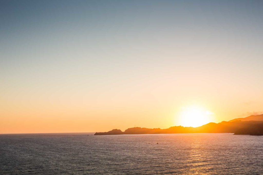 Sunset over a calm ocean with distant islands.
