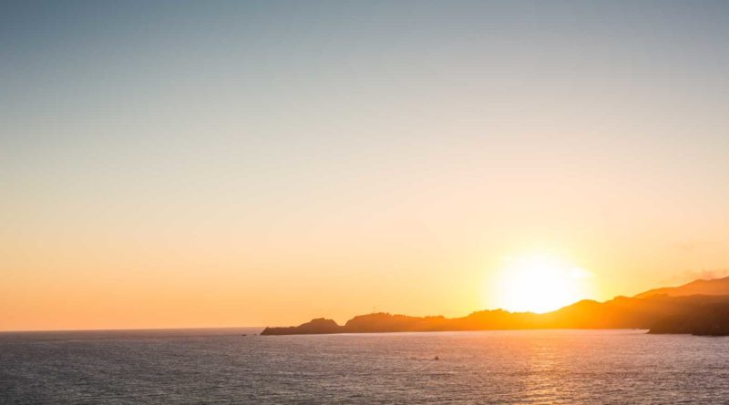 Sunset over a calm ocean with distant islands.