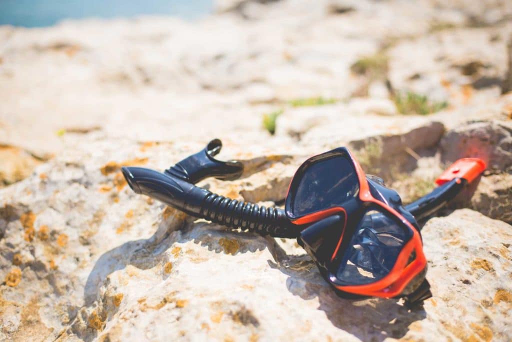 Black and red snorkel gear lying on rocky beach sand.