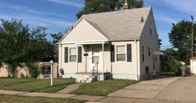 Small white house with a front porch and manicured lawn under blue sky.