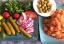 A plate of fresh vegetables, pickles, and olives.