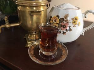 A glass of tea on a saucer with a floral teapot and brass samovar.