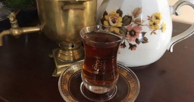 A glass of tea on a saucer with a floral teapot and brass samovar.