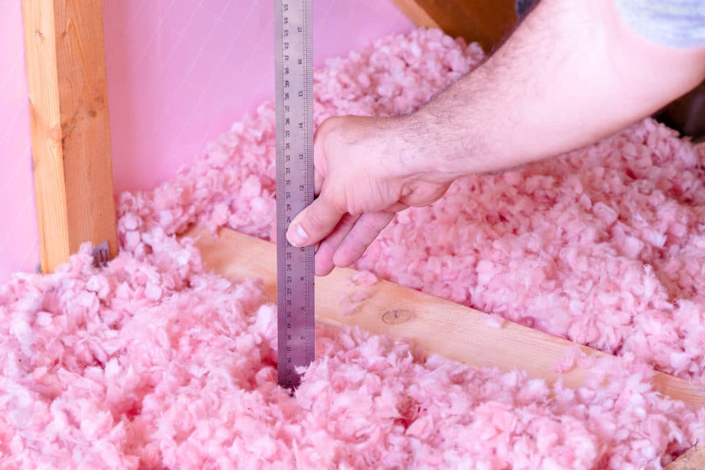 Hand measuring depth of pink foam beads with a ruler.