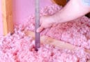 Hand measuring depth of pink foam beads with a ruler.