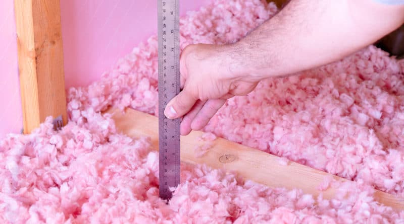 Hand measuring depth of pink foam beads with a ruler.