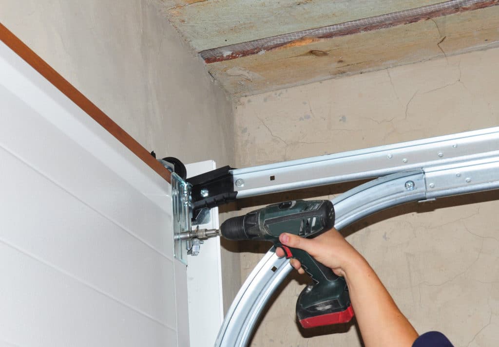 Person using a power drill to install a garage door hinge.