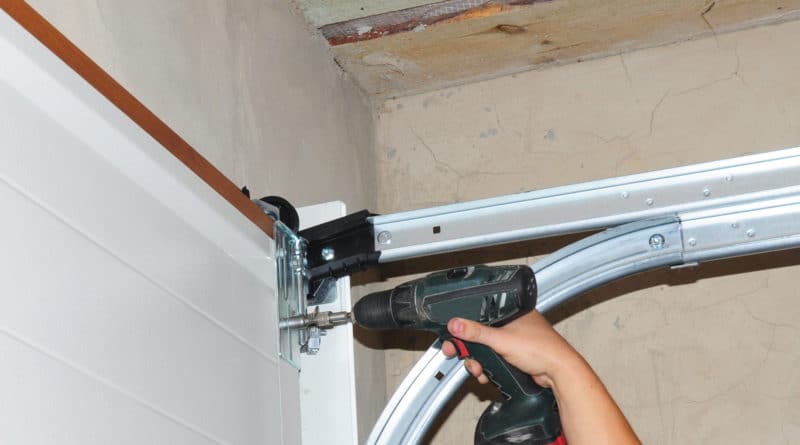 Person using a power drill to install a garage door hinge.