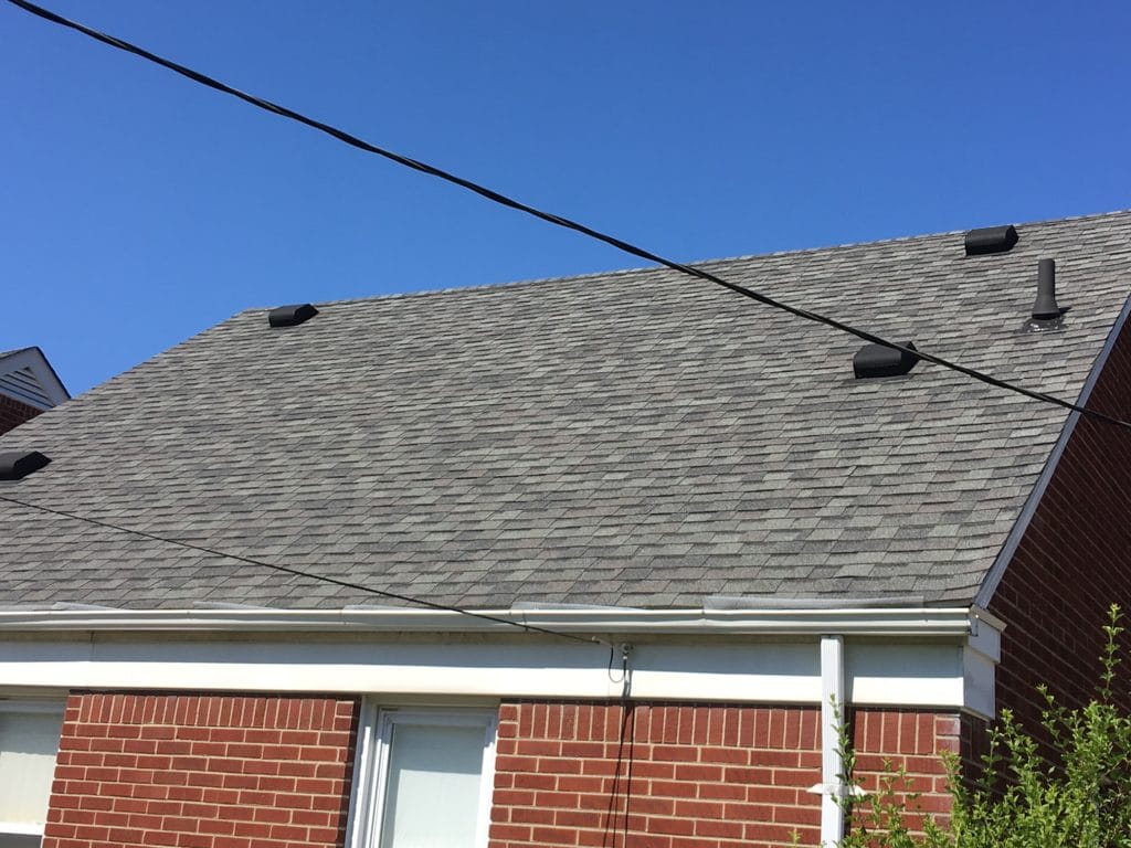 Roof of a brick house with gray shingles and utility wires.