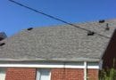 Roof of a brick house with gray shingles and utility wires.