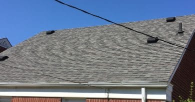 Roof of a brick house with gray shingles and utility wires.