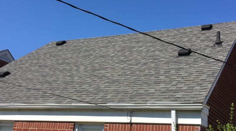 Roof of a brick house with gray shingles and utility wires.