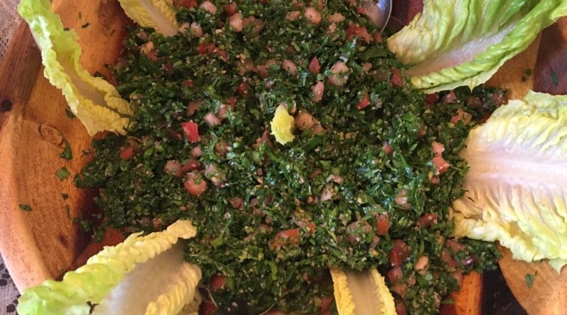 Fresh tabbouleh salad with lemon wedges and lettuce leaves.