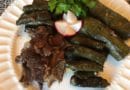 Grilled meat served with stuffed grape leaves and a radish garnish.