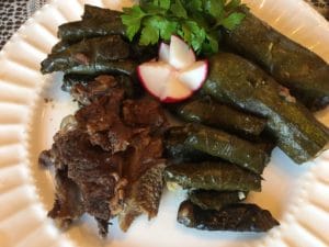 Grilled meat served with stuffed grape leaves and a radish garnish.