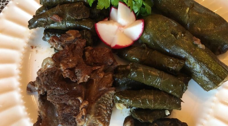 Grilled meat served with stuffed grape leaves and a radish garnish.