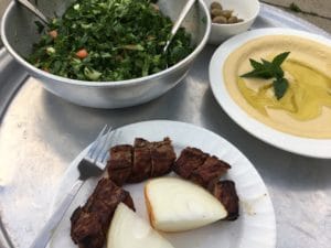 Grilled meat skewers served with onions, herbs, and a creamy dip.