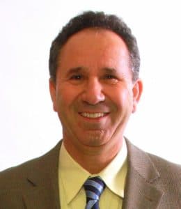 A smiling man in a suit and tie against a plain background.