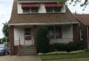 A modest brick house with a red awning and a trimmed shrub in front.