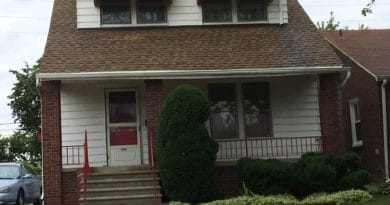 A modest brick house with a red awning and a trimmed shrub in front.
