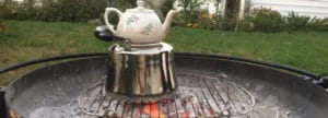 A teapot heating on a metallic stand over glowing charcoal.