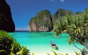 A tropical beach with clear turquoise water and a boat near lush cliffs.