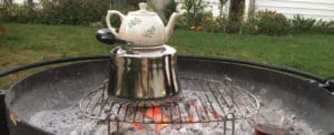 A teapot placed on a kettle over a grill with hot coals.