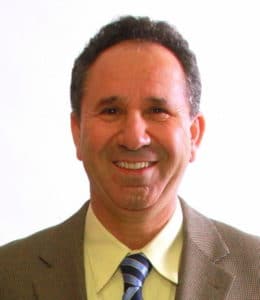 Smiling man in a suit and tie against a plain white background.