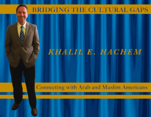 Man in suit standing by a banner about cultural connection with Arab and Muslim Americans.