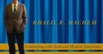 Man in suit standing by a banner about cultural connection with Arab and Muslim Americans.