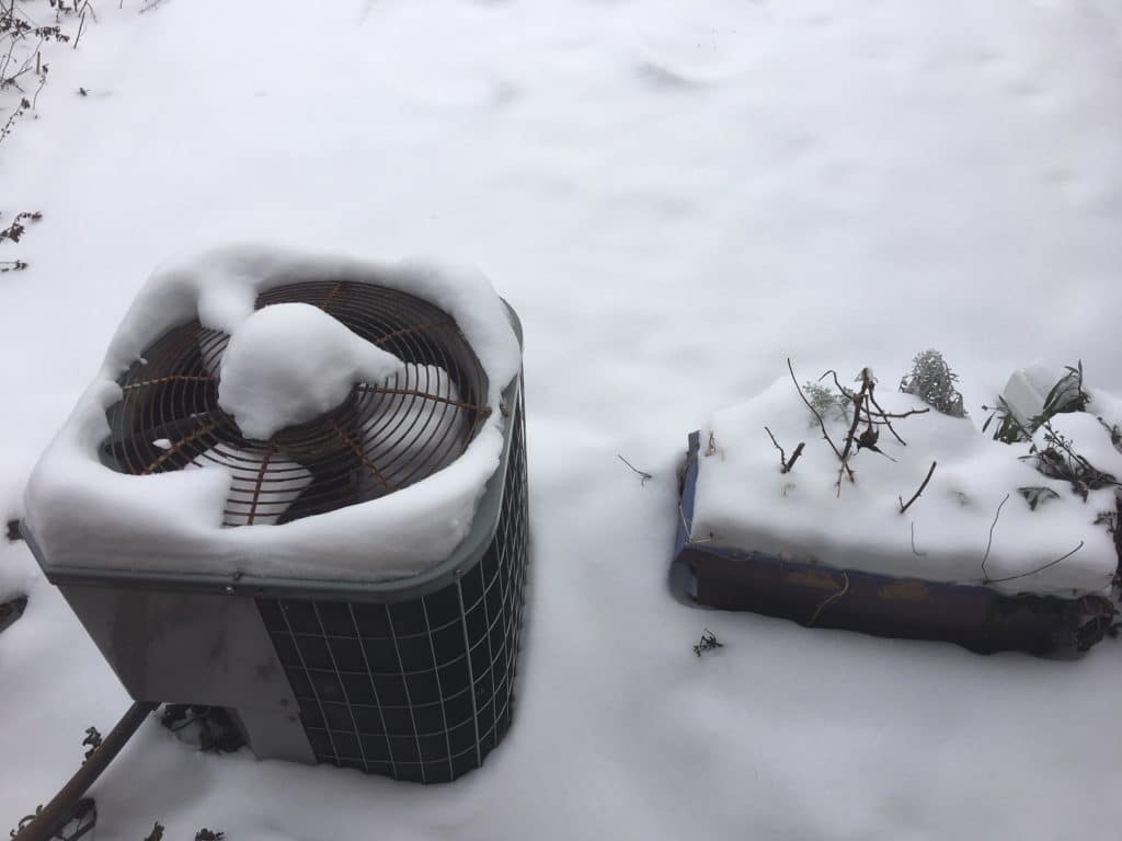 Outdoor HVAC unit covered in snow on a snowy day.