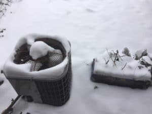 Outdoor HVAC unit covered in snow on a snowy day.