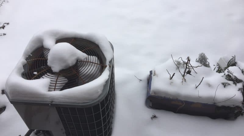 Outdoor HVAC unit covered in snow on a snowy day.