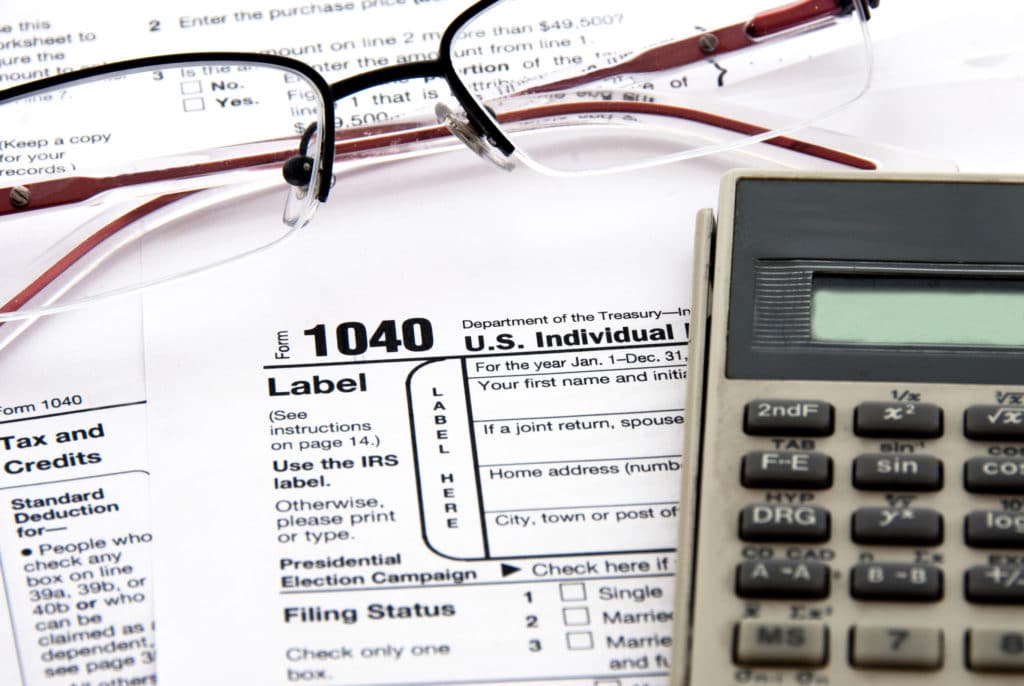 Tax form 1040, glasses, and calculator on a wooden desk.