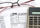 Tax form 1040, glasses, and calculator on a wooden desk.