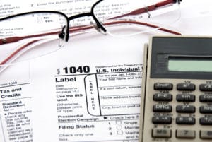 Tax form 1040, glasses, and calculator on a wooden desk.