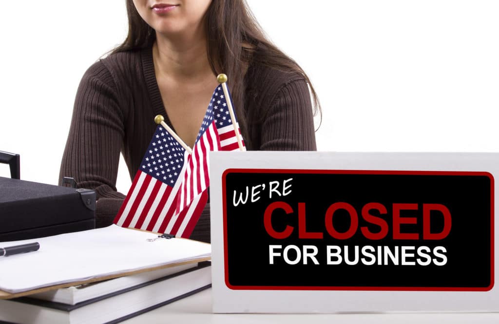Sign showing business closed with American flags in the background.