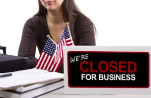 Sign showing business closed with American flags in the background.