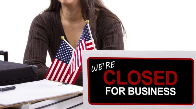 Sign showing business closed with American flags in the background.