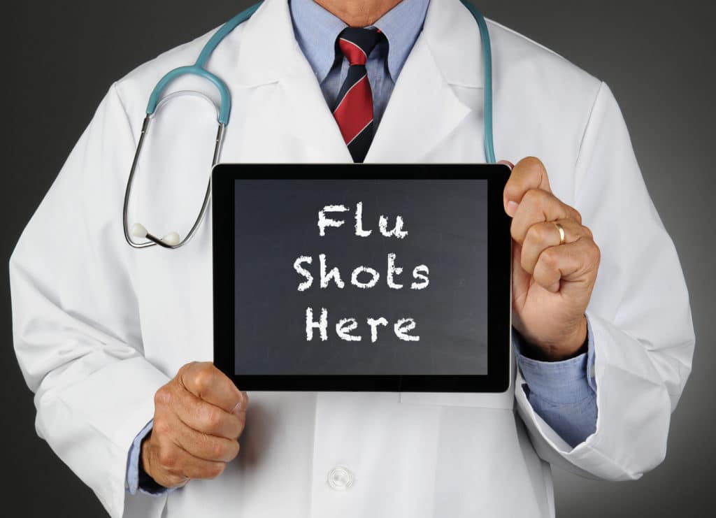 Doctor holding a sign that says 'Flu Shots Here'.