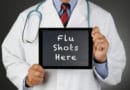 Doctor holding a sign that says 'Flu Shots Here'.