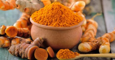 A bowl filled with bright orange turmeric powder with fresh turmeric roots around it.