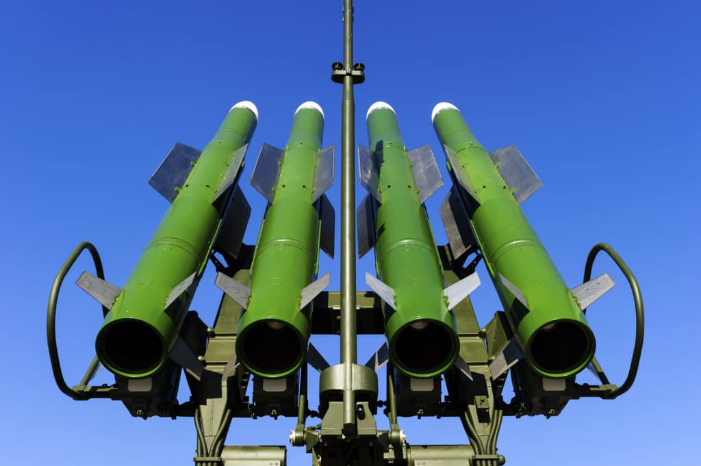 A close-up of green military missiles against a clear blue sky.