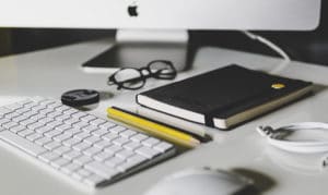 Desk setup with keyboard, glasses, notebook, and pencils.