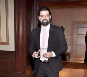 Man in a suit holding a drink at an indoor event.