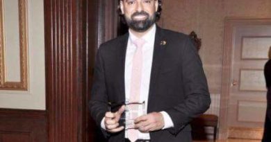 Man in a suit holding a drink at an indoor event.