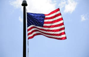 American flag waving on a flagpole against a blue sky.
